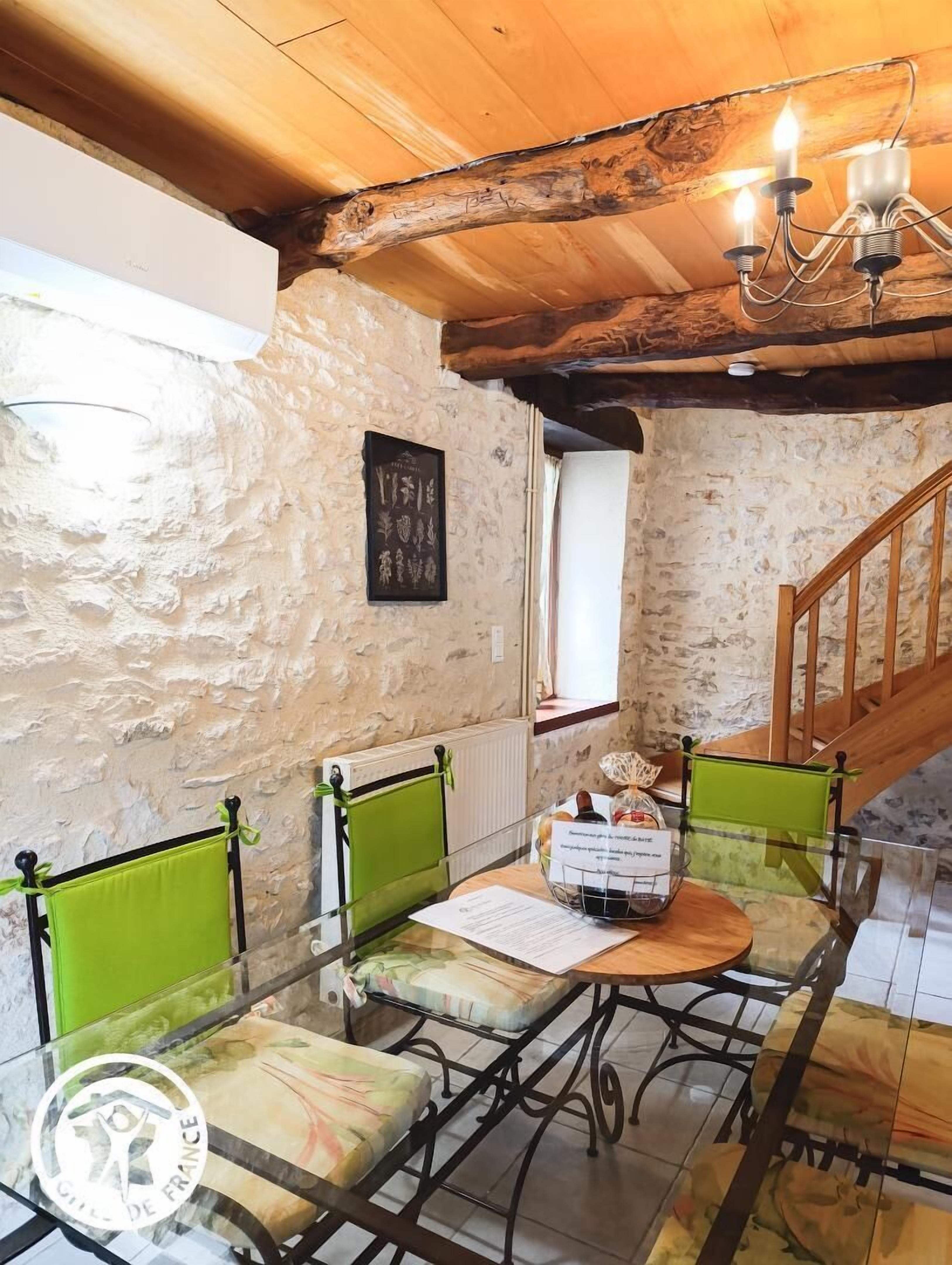 A rustic room with stone walls, a wooden ceiling, and a dining area with green chairs and a table.