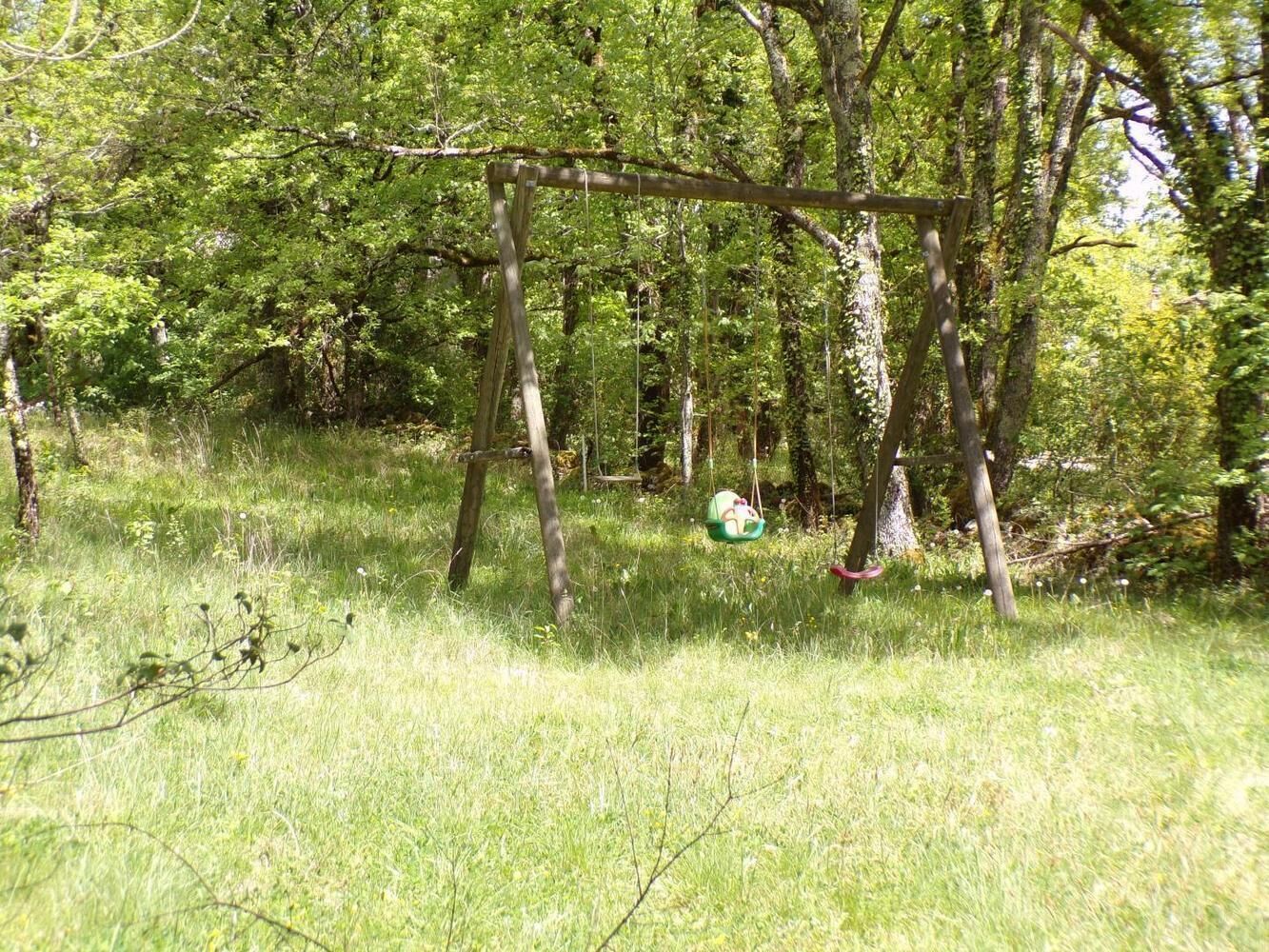 A wooden swing set in a grassy area with trees in the background.