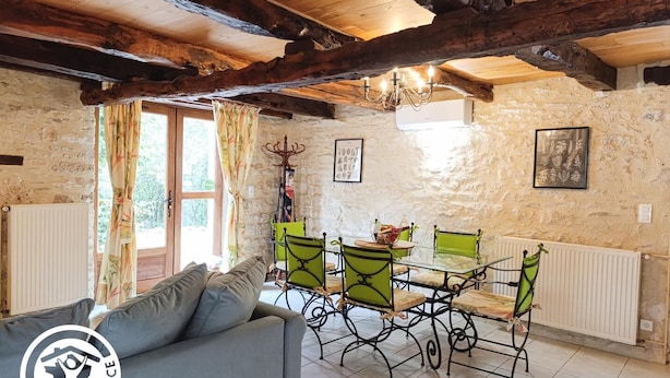 Ein rustikaler Raum mit freiliegenden Holzbalken, Steinwänden, einem Esstisch mit grünen Stühlen, einer Couch und einer Kristallleuchter.
