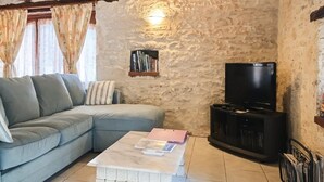 A cozy living room with a light blue sofa, a coffee table, a television, and a stone wall.