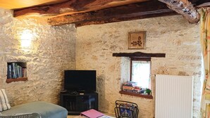 A rustic stone-walled room with a sofa, a television, and a radiator.