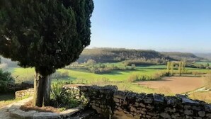 Eine Steinsichtmauer mit Stufen zu einer Steinsitzbank, umgeben von Grünpflanzen und mit freiem Blick auf eine hügelige Landschaft.