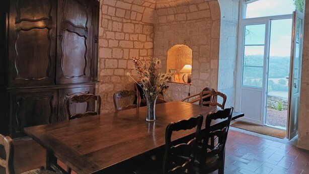 Ein Essbereich mit Holztisch und Stühlen, einer Vase mit Trockenblumen und einer Ziegelwand.