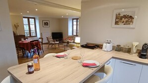 A dining area with a wooden table set for two, a bottle of wine, and a painting on the wall.
