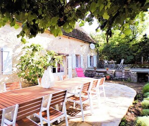 A stone building with a wooden table and chairs, a potted plant, and a stone fireplace.