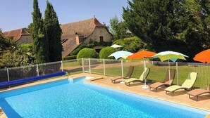 A swimming pool with lounge chairs and umbrellas, surrounded by a fence and trees. - Gîtes de France® - Le Poutoy (SAINT-SIMON)
