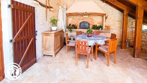 A rustic outdoor dining area with stone walls, wooden furniture, and a fireplace. - Gîtes de France® - Le Poutoy (SAINT-SIMON)