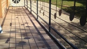 Een houten terras met een metalen hekwerk, een vredesteken en muzieknoten op de grond.