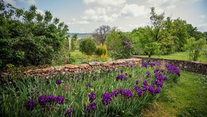 A garden with a stone wall and purple flowers. - Gîtes de France® - LE MAS D'AYRENS (FIGEAC)