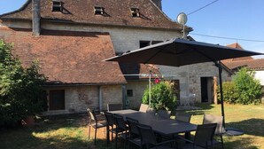 A rustic stone house with a tiled roof, a patio with a table and chairs, and a satellite dish. - Gîtes de France® - Gîte Le Cammas (SAINT SIMON)