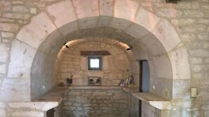 A stone-walled room with a small window, a shelf with books, and a stone bench. - Gîtes de France® - Gîte Le Cammas (SAINT SIMON)
