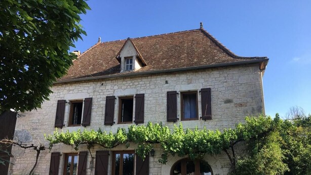 A two-story stone building with a tiled roof, multiple windows with shutters, and a vine-covered front. - Gîtes de France® - Gîte Le Cammas (SAINT SIMON)