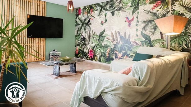 Et værelse med tropisk tapet, et fladskærms-tv, en væg med trælameller, en bænk og en seng med lampe.