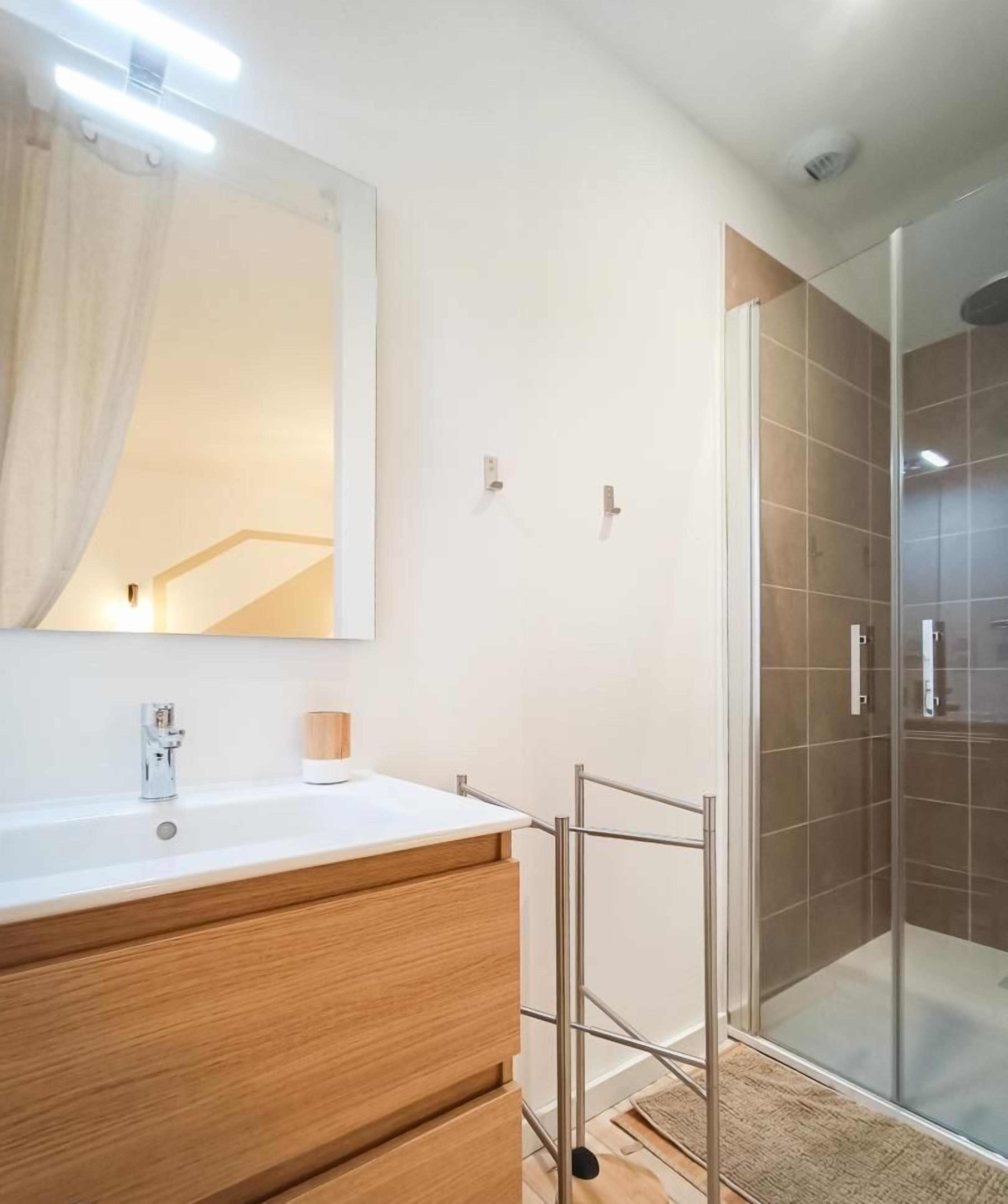 A modern bathroom with a wooden vanity, a large mirror, and a glass shower enclosure.