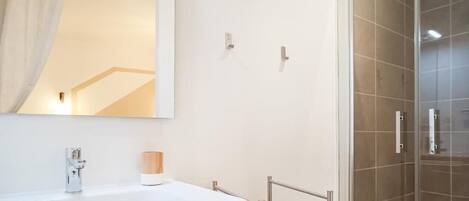 A modern bathroom with a wooden vanity, a large mirror, and a glass shower enclosure.