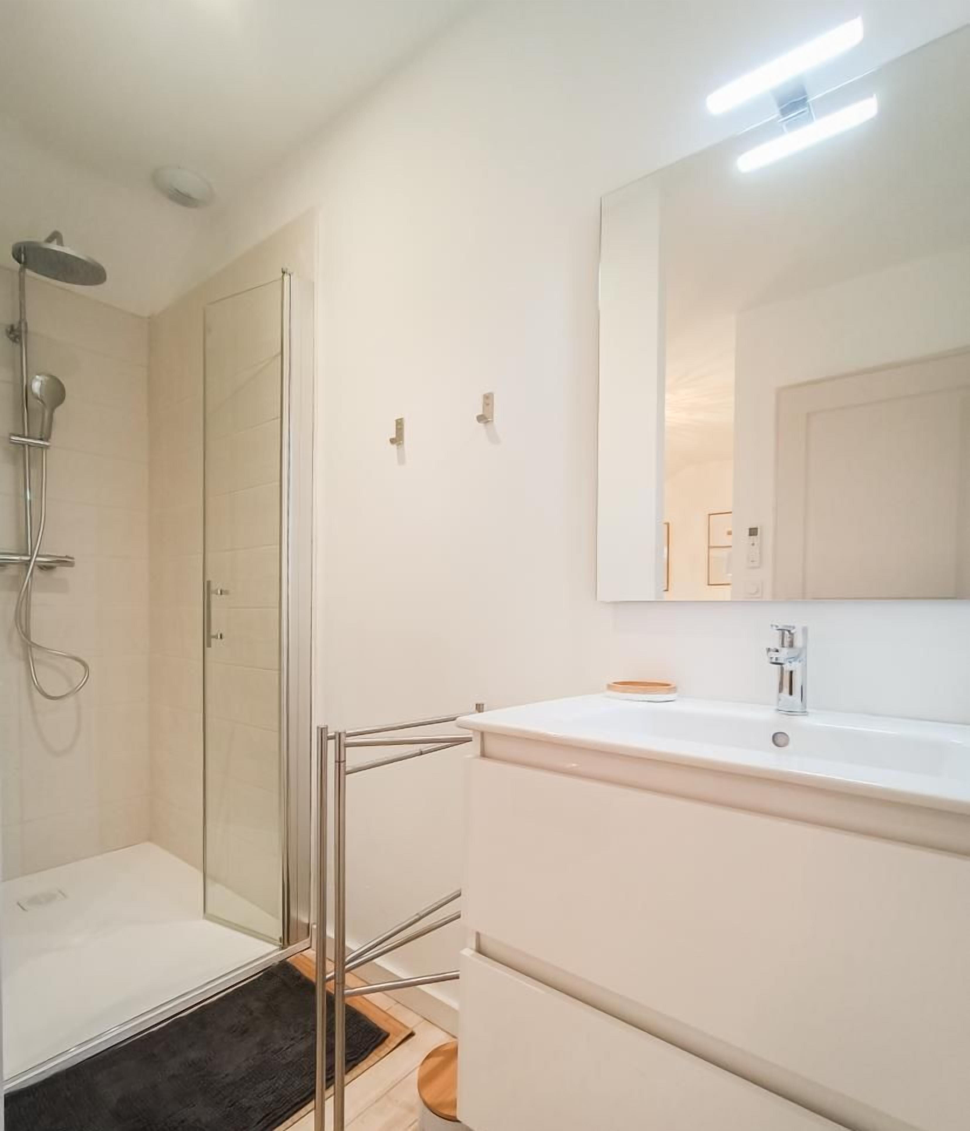 A modern bathroom with a glass shower enclosure, a white vanity with a mirror, and a tiled floor.