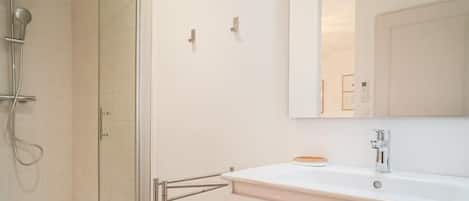 A modern bathroom with a glass shower enclosure, a white vanity with a mirror, and a tiled floor.