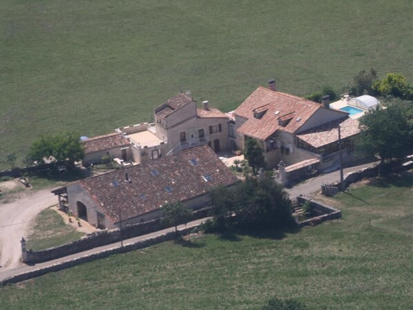 An aerial view of a rural property with a large building, a swimming pool, and surrounding greenery.