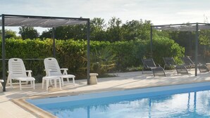 Una piscina con sillas de descanso y una pérgola.