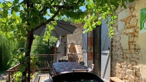 A patio area with a grill, outdoor seating, and a stone wall. - Gîtes de France® - Le Fournil (GIGOUZAC)