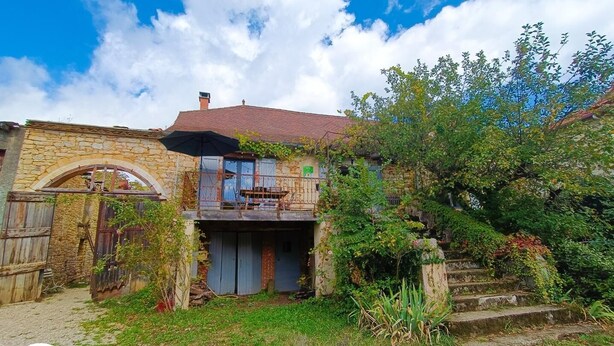 A rustic stone house with a tiled roof, a balcony, and a small garden area. - Gîtes de France® - Le Fournil (GIGOUZAC)