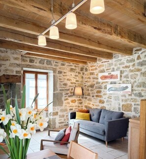 A rustic interior with exposed wooden beams, a stone wall, a sofa, and a vase of flowers.