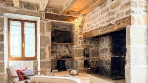 Una habitación con paredes de piedra, chimenea, televisor y un rincón de estar con cojines.