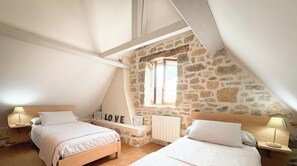 A bedroom with two beds, stone walls, a sloped ceiling, and a window.