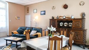 A living room with a sofa, dining table, chairs, and a wooden cabinet with decorative items.