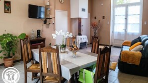 A dining area with a table set for four, surrounded by wooden chairs with woven seats. A television is mounted on the wall above the table.