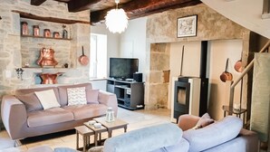 A cozy living room with a stone wall, a fireplace, a television, and a sofa. - Gîtes de France® - La Caze (ALVIGNAC LES EAUX)