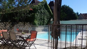A poolside area with a table and chairs, a stone wall, and a view of a swimming pool. - Gîtes de France® - La Caze (ALVIGNAC LES EAUX)