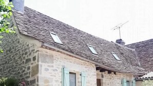 A stone building with a tiled roof, a small staircase leading to the entrance, and a door with a green sign. - Gîtes de France® - La Caze (ALVIGNAC LES EAUX)