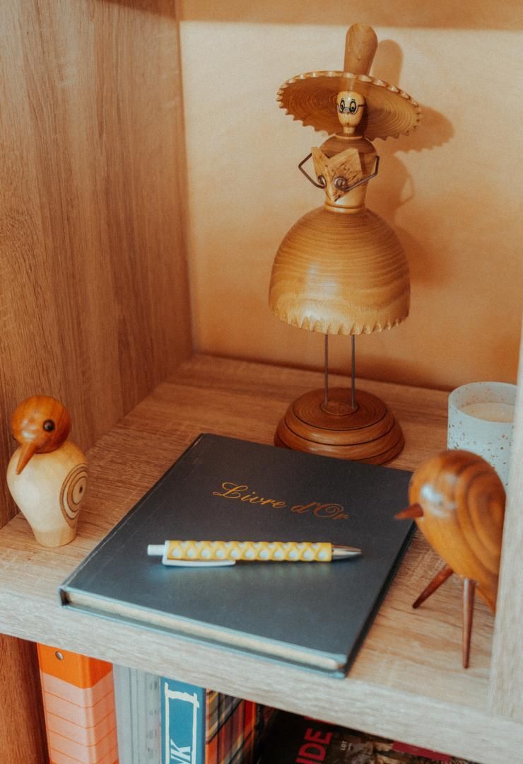 A wooden shelf with a decorative wooden figure, a book titled 'Live d'Or,' and a pen.