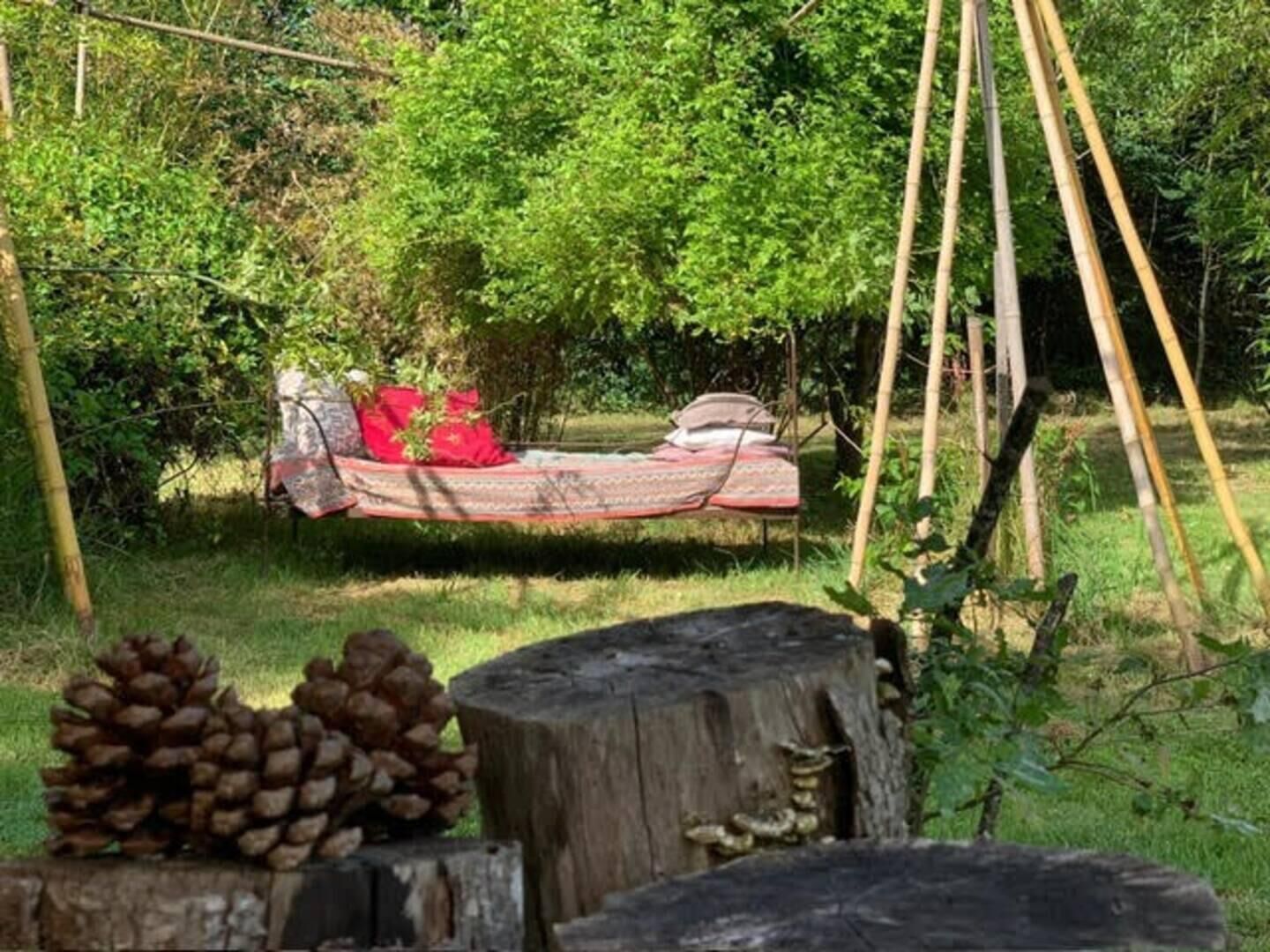 A hammock bed in a natural setting with a wooden post and a tree stump nearby.