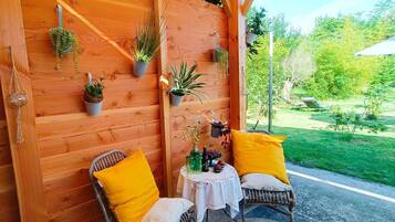 Eine Holzwand mit Topfpflanzen, zwei Korbstühle mit gelben Kissen und ein kleiner Tisch mit weißem Tuch.