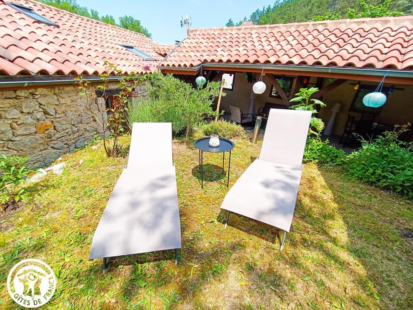 A courtyard with two lounge chairs, a small table, and a stone wall.