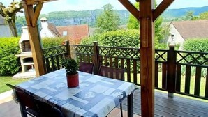 En uteplats med ett träbord och stolar, en krukväxt och utsikt över landskapet.
