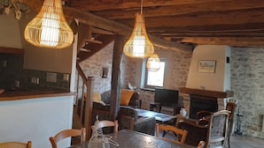 A rustic interior with exposed wooden beams, a stone fireplace, and a dining area with wooden chairs and a table. - Gîtes de France® - LES CIGALES (SAINT-SOZY)