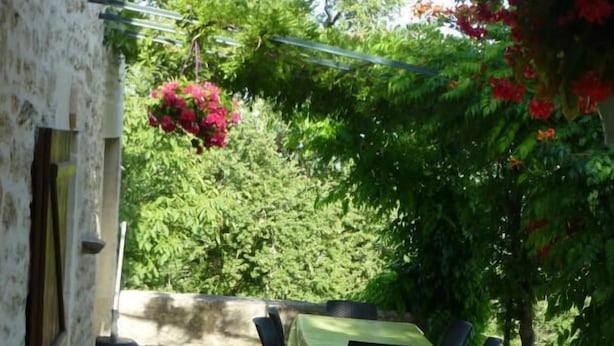 A stone patio with a table and chairs, surrounded by greenery and flowering plants. - Gîtes de France® - LES CIGALES (SAINT-SOZY)
