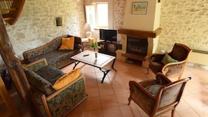 A cozy living room with a stone wall, a fireplace, a sofa, and a television. - Gîtes de France® - LES CIGALES (SAINT-SOZY)