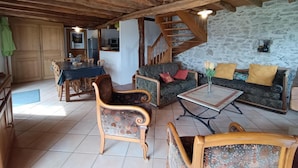 A rustic interior with wooden beams, a dining area, a sofa set, and a staircase. - Gîtes de France® - LES CIGALES (SAINT-SOZY)