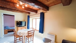 A cozy room with a wooden ceiling, a dining table with chairs, a TV, and a window with curtains.