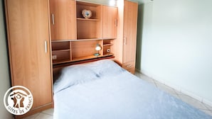 A bedroom with wooden cabinets, a bed, and a small table with a lamp.
