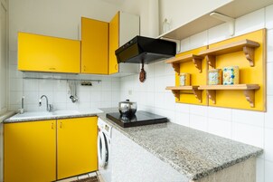 Una cocina con armarios amarillos, campana extractora negra, encimera de granito y estantes de madera con objetos decorativos.