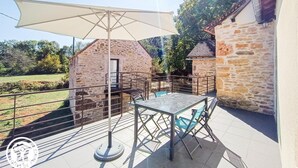 A patio with a table and chairs, a large umbrella, and a stone building in the background.