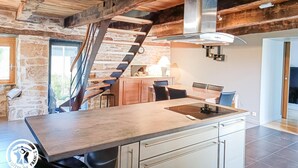 A modern kitchen with a central island, wooden beams, and a stone wall.