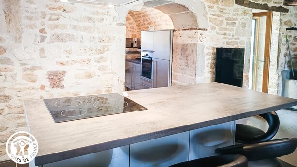 A kitchen with a stone wall, a modern gas stove, and a wooden ceiling.