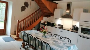 Eine Küche mit einer Holztreppe, einem Esstisch mit Stühlen und einer Pendelleuchte.
