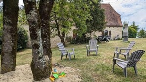 Ein Garten mit einem Steinhaus, Gartenstühlen und einem Baum.